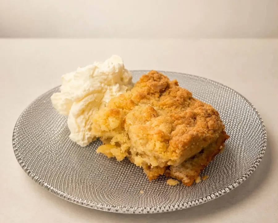 A portion of apple cake on a plate with whipped cream